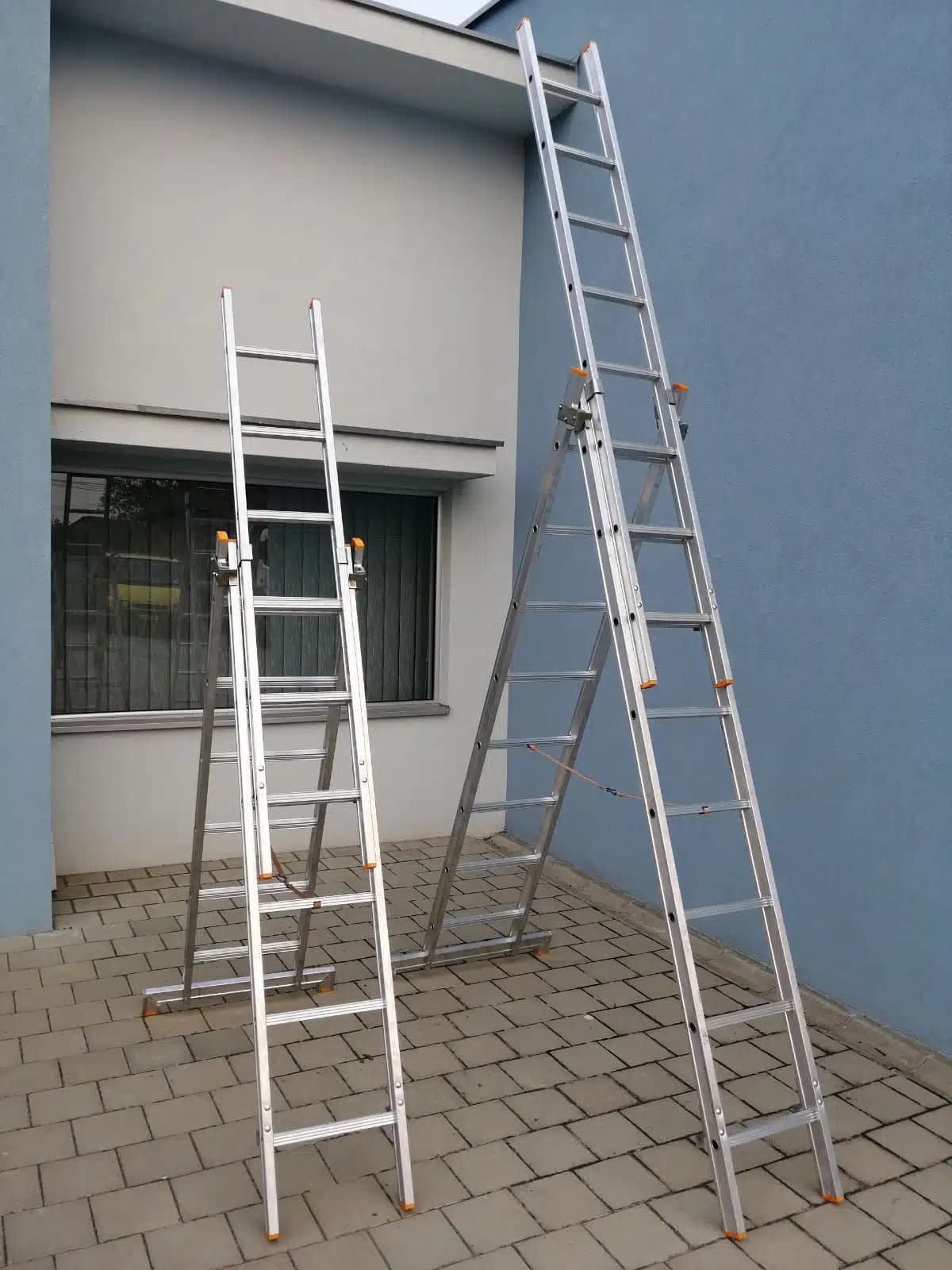 Two aluminium three-section ladders leaning against a building wall